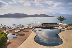 伊罗达Domes Aulus Elounda All-Inclusive Resort, Curio by Hilton的水边带椅子和遮阳伞的游泳池