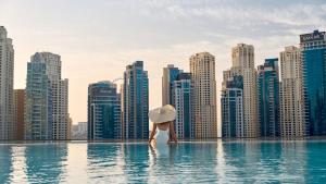 迪拜Luxurious 2BR apt with panoramic Marina view的城市天际线的无边游泳池中的女人