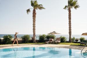 玛利亚Ikaros Beach, Luxury Resort & Spa - Adults Only的一位女士在棕榈树游泳池旁散步