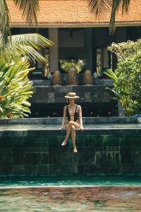 会安Almanity Hoi An Resort & Spa的坐在游泳池边戴帽子的女人