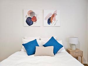 悉尼Cosy 3BR House, 7 mins drive to Macquarie Centre, 5 stars on AirB&B的一张带蓝色枕头的白色床和墙上的三张照片