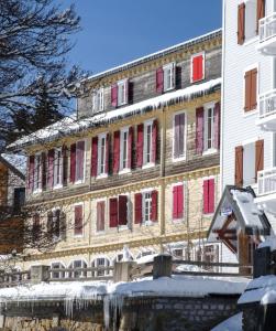 Pugny-ChatenodLocation montagne le Revard的一座大建筑,在雪中装有红色百叶窗