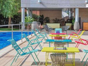 科尔内拉德罗布雷加特诺富特巴塞罗那科内拉酒店的一组五颜六色的桌子和椅子,旁边是游泳池