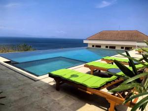 珀尼达岛Jukung Dive Resort Bali PENIDA的一个带绿色躺椅的游泳池以及大海