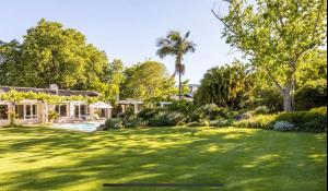 开普敦Garden Cottage - Leafy Constantia Guest House的一个带大草坪的院子,里面种有树木,还有房子