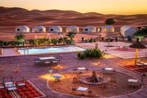 梅尔祖卡Yakout Merzouga Luxury Camp的沙漠中的度假村,设有游泳池和桌子