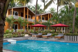 莫尔吉姆Aralea Beach Resort By Stone Wood, Morjim的一个带椅子和遮阳伞的游泳池的度假酒店