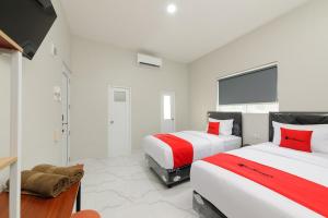 HajimanaRedDoorz near GSG UNILA Lampung的配有白色墙壁和红色色调的客房内的两张床