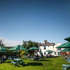 英格尔顿The Wheatsheaf Inn的一组野餐桌和绿色雨伞