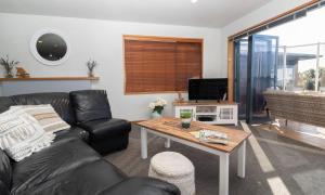 新普利茅斯Beachfront Bliss On Wanaka Terrace Support Local的客厅配有黑色真皮沙发和桌子