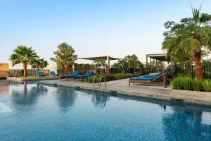 迪拜Radisson Dubai Damac Hills的游泳池拥有蓝色长椅和棕榈树