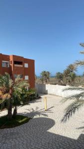 Jāmi‘ al GuelloufiAppartement T3 proche de la Plage !的棕榈树海滩上的一座建筑和人行道