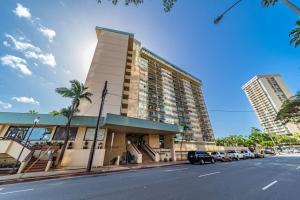 檀香山Waikiki Beach Golden Holiday的一座高大的建筑,前面有汽车停放