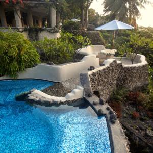 塔纳岛Rockwater Resort的一座带遮阳伞的游泳池位于度假酒店旁