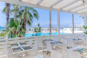 托雷圣乔万尼乌Villaggio Poseidone Beach Resort - Hotel的一间带白色桌椅的餐厅和一个游泳池