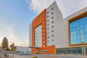 莱昂City Express Junior by Marriott Leon Centro de Convenciones的一座橙色和白色的酒店大楼,设有停车场
