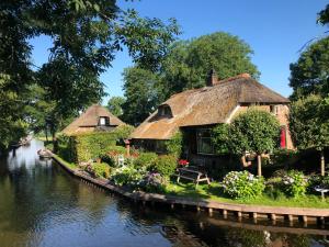 羊角村Plompeblad Suite Giethoorn的运河旁的几栋茅草小屋