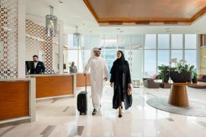 多哈Delta Hotels by Marriott City Center Doha的带着手提箱在机场走的男人和女人