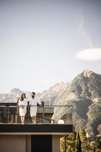 蒂鲁罗Vinea - Apartments的两名女性在阳台散步,阳台背景是山脉