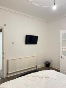 伦敦StayEasy En-Suite London的一间白色墙壁上配有电视的卧室