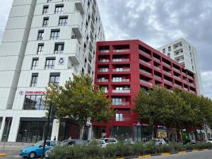 地拉那Urbanin Apartment & Hotel的一座红色的公寓楼,前面有汽车停放