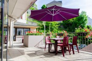 卢尔德Hôtel Hélianthe的庭院内一张桌子和椅子,上面配有紫色雨伞