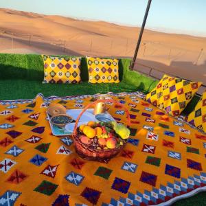 Al WāşilBidiya Dunes camp عزبة بدية ديونز的一张桌子,上面有一篮水果放在毯子上