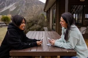 库克山村Haka House Aoraki Mt Cook的两个坐在野餐桌旁看手机的女人