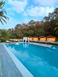 丹德利Stone Wood Jungle Resort, Dandeli的一座大型蓝色游泳池,设有一排小屋