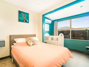 怀蒂昂格Acacia Cote - Whitianga Holiday Home的一间卧室设有一张婴儿床和大窗户