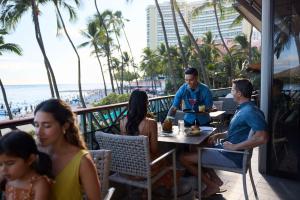 檀香山OUTRIGGER Waikiki Beach Resort的一群人坐在海滩上的一家餐馆的桌子上