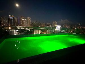 马尼拉City Nest Makati with Rooftop pool and Free Netflix的一座绿色的游泳池,晚上享有城市天际线