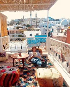 丹吉尔The Riad Hostel Tangier的坐在阳台上的女人,坐在阳台上,边喝咖啡