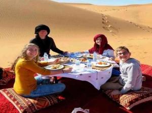 梅尔祖卡Merzouga Top Luxury Camp的一群人坐在沙漠的桌子旁
