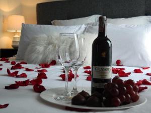 OcañaHotel Boutique Doña Maria的床上的一瓶葡萄酒和玻璃杯,配红玫瑰