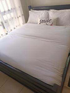内罗毕Blue Falls Queen Studio的一张带白色床单和微笑枕头的床