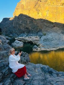 马斯喀特Wadi Al Arbeieen Resort的坐在岩石上拍着水景的女人