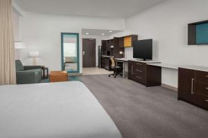 奥兰多Home2 Suites Orlando Southeast Nona的酒店客房配有一张床和一张书桌及一台电视