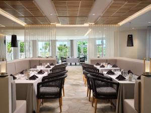 可可比奇Hilton Garden Inn Cocoa Beach-Oceanfront, FL的餐厅设有白色的桌椅和窗户。