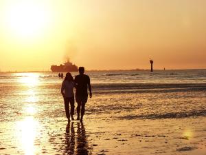 奥特尔恩多夫Ferienhaus Wattwurm的日落时在海滩上散步的男人和女人