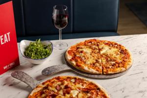 达宁顿堡Leonardo Hotel East Midlands Airport的坐在桌子上的两份比萨饼,佐以一杯葡萄酒