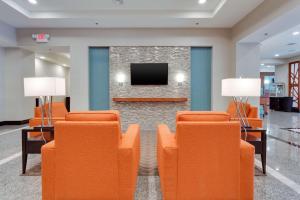 迈尔斯堡Drury Inn & Suites Fort Myers Airport FGCU的一间配备有橙色椅子和电视的等候室