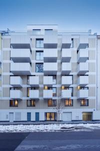 维也纳Zoder Apartments的雪中公寓楼,前面有一棵树