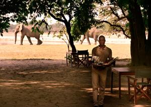 KakumbiMsandile River Lodge的一位在桌子前行走的男人,身后有大象