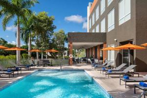 蓬塔卡纳福朋喜来登蓬塔卡纳村酒店的酒店旁的游泳池配有椅子和遮阳伞