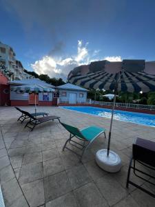 拉特里尼泰Ananas Premium的一个带两把椅子和一把遮阳伞的庭院,毗邻一个游泳池