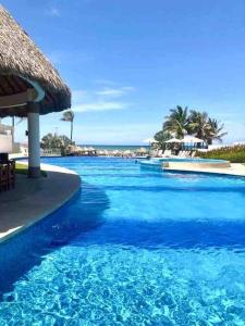 阿卡普尔科Hermoso Apartamento con club de playa的一个带草伞的大型蓝色游泳池