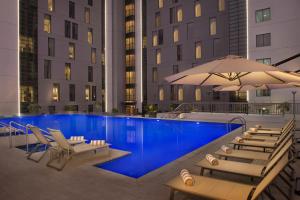 迪拜迪拜机场汉普顿酒店 的一个带椅子和遮阳伞的游泳池