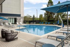 奥兰多Home2 Suites Orlando Southeast Nona的甲板上配有椅子和遮阳伞的游泳池