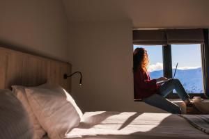 古多里Alpina Hotel的坐在床上看着窗外的女人